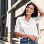 A smiling woman wearing a white button up shirt poses in a city alley.