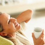 Woman relaxing on a green sofa with a cup of tea.